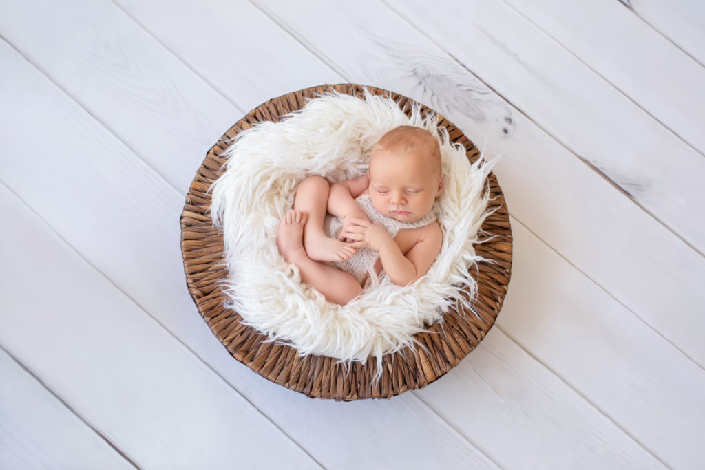 Newborn baby boy Ezra sleeping on white fur in brown basket Gainesville Florida newborn photographer