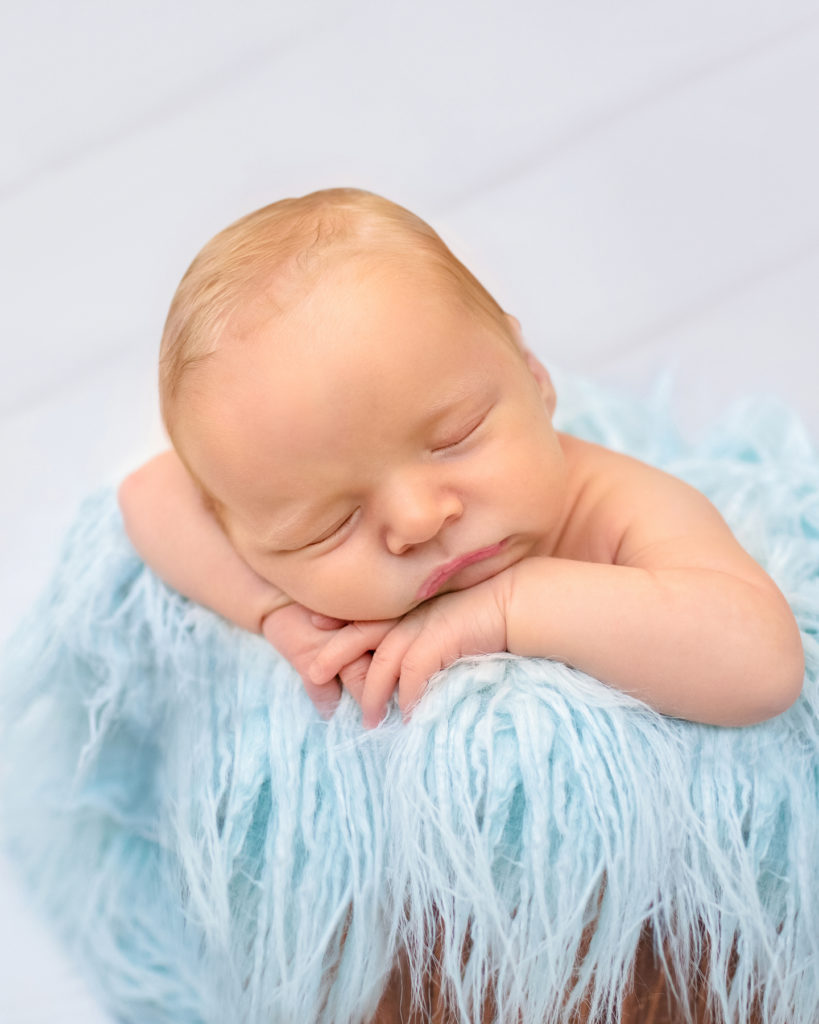 Newborn baby boy Ezra sleeping with his chin on his wrists in fur stuffed bucket Gainesville Florida newborn photographer