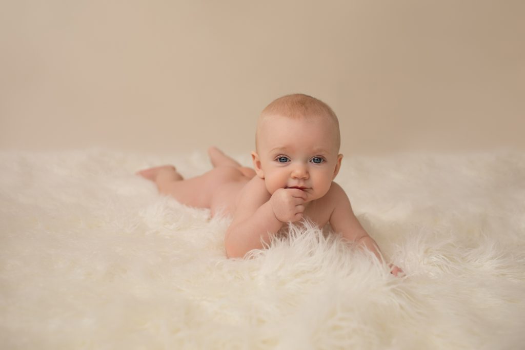 six month naked baby Rachel with soft baby skin posed beautifully on white fur lying on her tummy