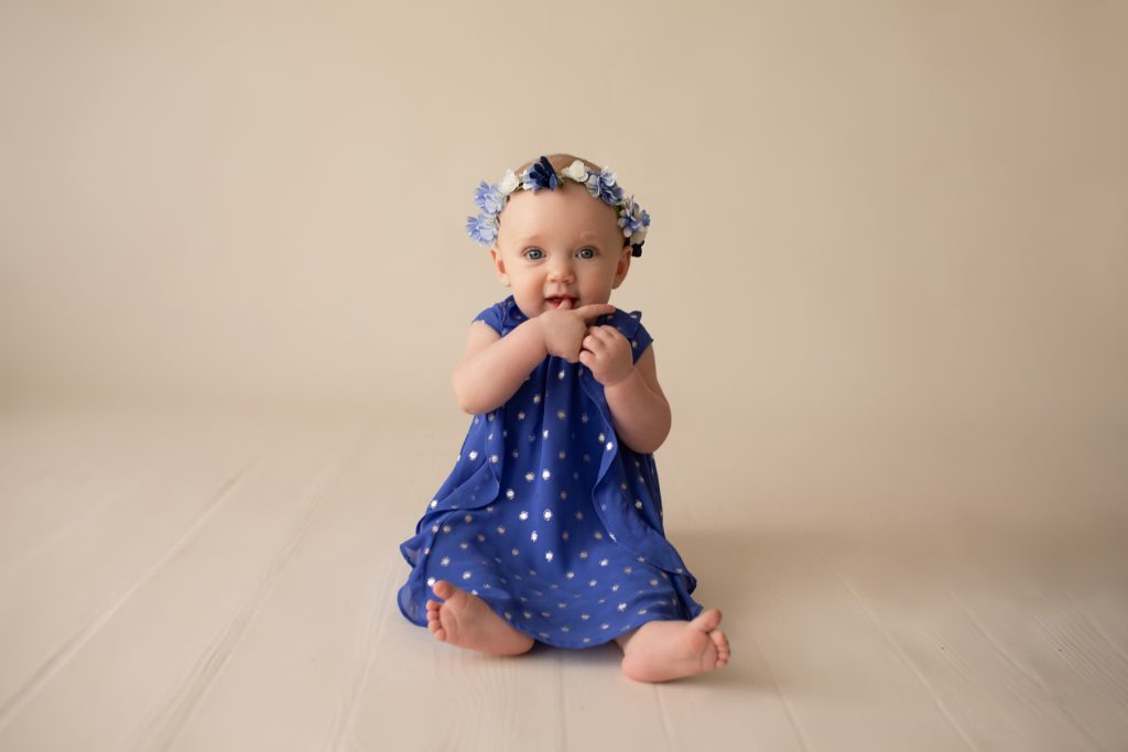 beautiful baby photos 6 month girl wears blue polka dot dress and floral crown hands in mouth