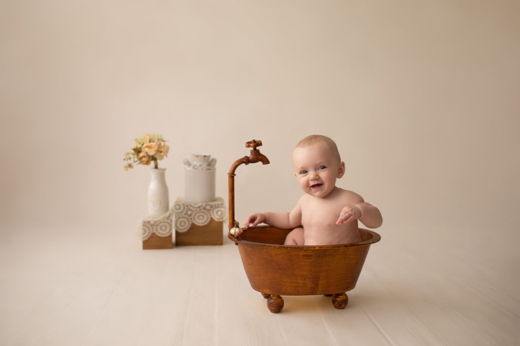 six month naked baby Rachel smiles with personality sitting in brown old fashioned tub playing peek