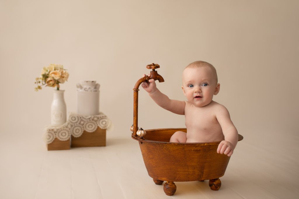 six month naked baby Rachel smiles with personality sitting in brown old fashioned tub