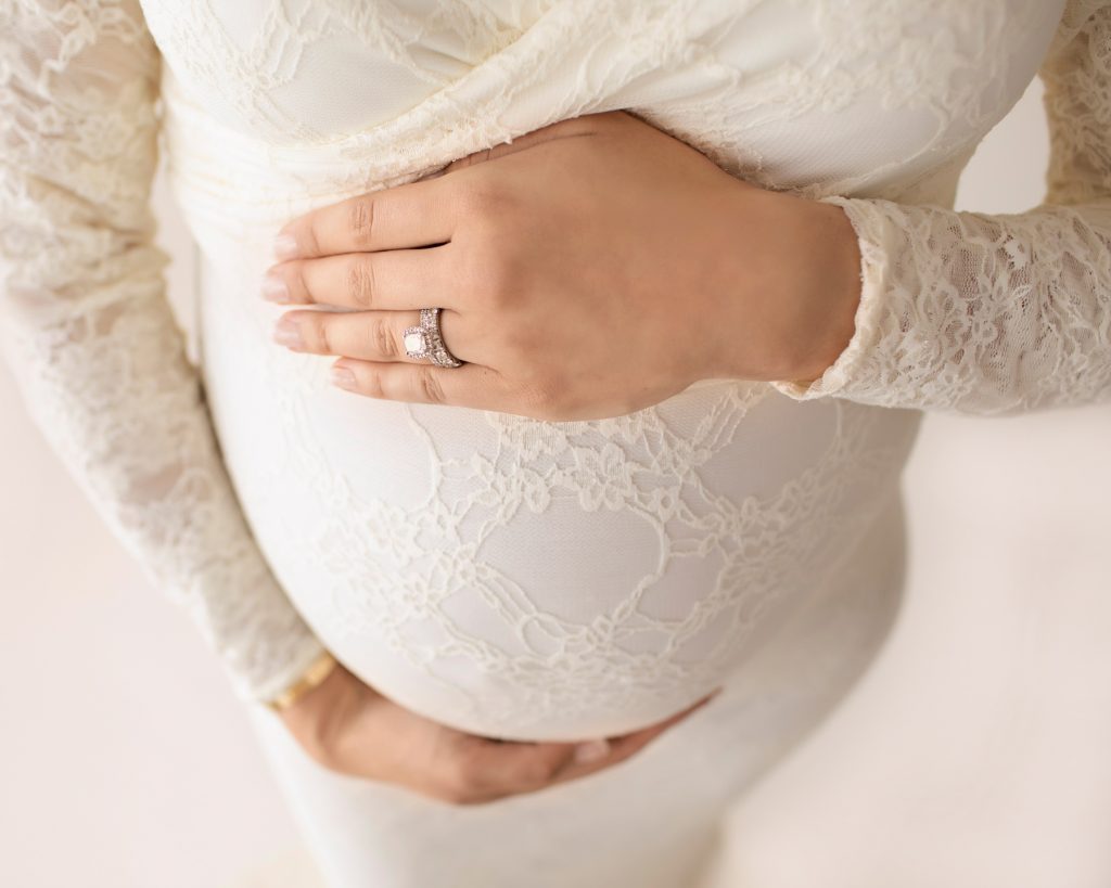 Gorgeous pregnant mom dressed in long sleeved ivory lace mermaid maternity gown holding beautiful baby belly with both hands