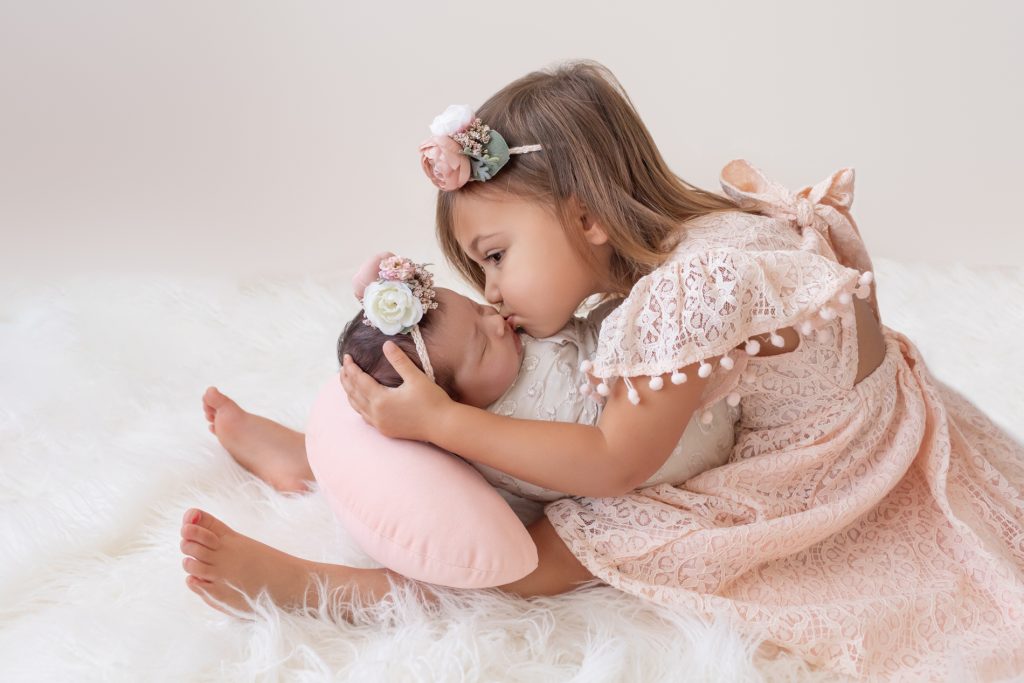 Big Sister Kisses Newborn Baby Sister on Forehead